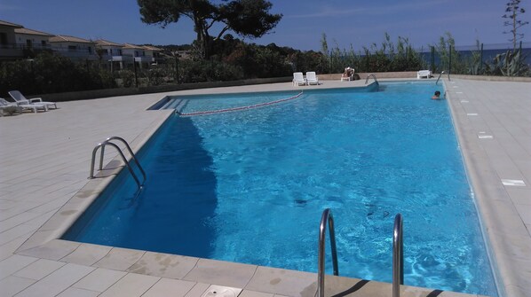 A rectangular swimming pool with clear blue water, surrounded by a tiled deck. There are lounge chairs and a small table on the deck. - Santa Lucia, Unit 357 (Santa-Lucia-Di-Moriani)