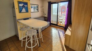 A compact dining area with a white table and four chairs, a small bench, and a view through a glass door to an outdoor patio. - Beautiful appartment with sea view and near of the beach (SIX FOURS LES PLAGES)