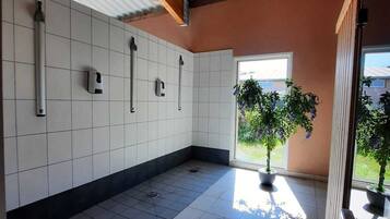 Une cuisine spacieuse avec des murs recouverts de carreaux blancs, un sol carrelé et un plafond en bois. On y trouve trois robinets fixés au mur et une plante en pot près de la fenêtre.