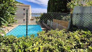 A swimming pool surrounded by a chain-link fence, with a tall tree and a building in the background. - Garden with barbecue, swimming pool (LA SEYNE SUR MER)