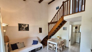 A cozy living room with a sofa, a dining table, and a wooden staircase. - Garden with barbecue, swimming pool (LA SEYNE SUR MER)