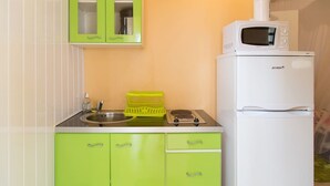 Une cuisine de taille réduite avec des meubles verts, un réfrigérateur blanc, un four à micro-ondes et une cuisinière à gaz.