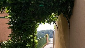 A narrow concrete pathway flanked by a wall and a metal fence, with a green bush growing along the wall. - T2 1 bedroom 4 people for rent 83700 Saint Raphaël / Le Dramont  (Saint-Raphaël)