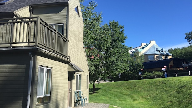 A two-story house with a balcony, a small porch with chairs, and a grassy yard with stepping stones. - Perfect Location / Perfectly Located Ski-in / Ski-out  (Mont-Tremblant)