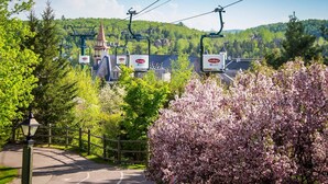 A ski lift with a sign for a ski resort, surrounded by blooming trees and a mountain backdrop. - Perfect Location / Perfectly Located Ski-in / Ski-out  (Mont-Tremblant)