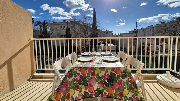 Ein Balkon mit Esstisch für vier Personen, Blick auf ein Wohngebiet mit Häusern und blauem Himmel.