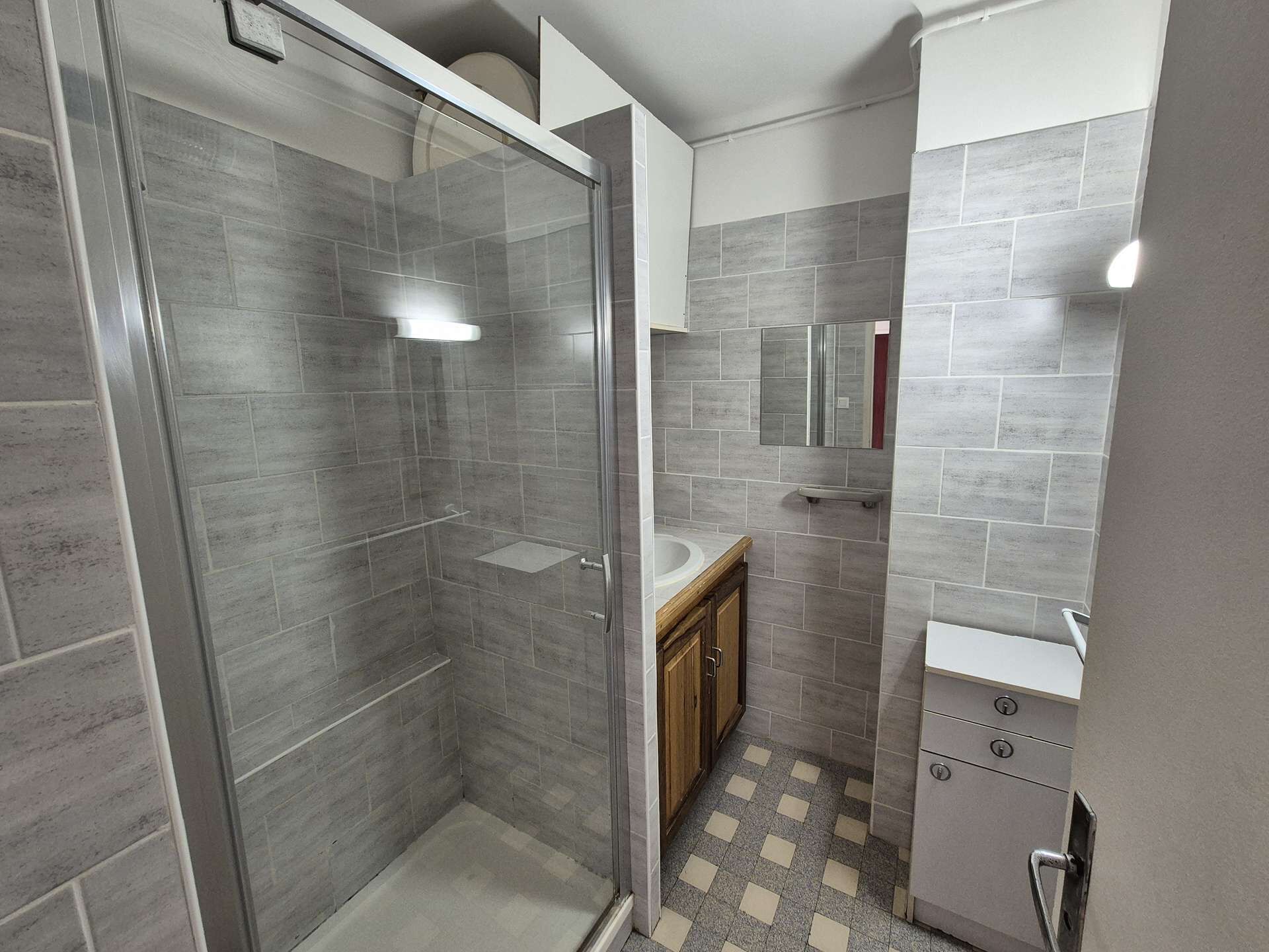 A modern bathroom with a glass-enclosed shower, a wooden vanity, and a tiled floor.