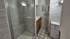 Ein modernes Badezimmer mit einer gläsernen Duschkabine, einem hölzernen Waschtisch und einem gefliesten Boden.