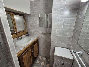Een compacte badkamer met een houten wastafelmeubel, een witte wasbak en een klein wit toilet.