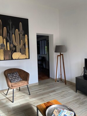 A modern living room with a large abstract painting, a brown armchair, a coffee table, a floor lamp, and a television.