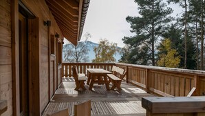 Terraza de madera con mesa y sillas, con vista a un paisaje montañoso.