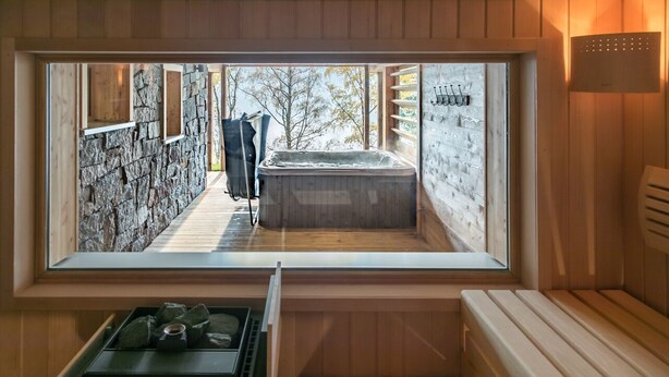 Una sauna con pared de piedra, banco de madera y ventana con vistas a un sendero de piedra.