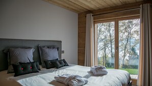 Un dormitorio con una cama grande, almohadas grises y negras, y vistas a árboles a través de la ventana.