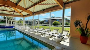 Piscina con sillones de descanso y una zona cubierta con ventanas amplias.