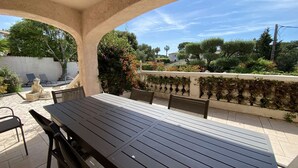 Patio esterno con tavolo e sedie, circondato da un muro bianco con vegetazione e vista su alberi ed edifici.