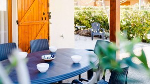 Ein runder Tisch mit Stühlen und Schüsseln, eine Holztür und Blick auf einen Garten mit Stuhl und Tisch.