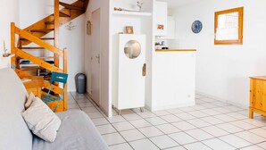 Ein kompakter Wohnraum mit Treppe, einem weißen Kühlschrank, einem Holzschrank und einem Fliesenboden.