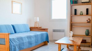 A room with a blue sofa, a wooden table, a bookshelf, and a window.