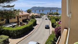 Une rue résidentielle bordée de maisons, avec des voitures garées, et offrant une vue dégagée sur la mer et les montagnes en arrière-plan.