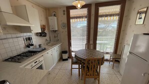 Une cuisine de taille réduite, équipée d’une cuisinière à gaz, de meubles blancs, d’une table à manger en bois et d’un réfrigérateur.