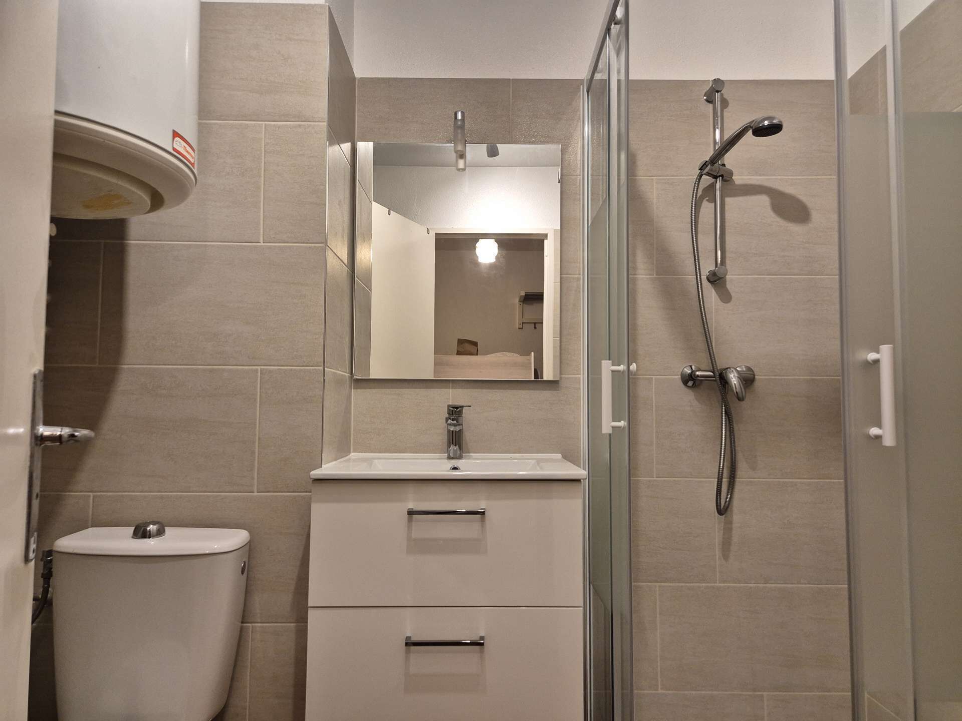 A modern bathroom with a toilet, sink, mirror, and shower.