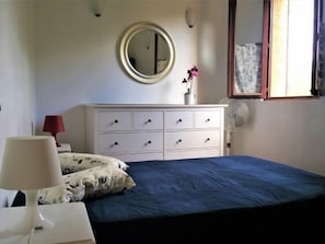 A bedroom with a bed, a dresser, a mirror, a lamp, and a window. - Corse House 6 pers wide garden 200m beach Calvi (Calvi)