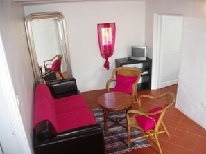 A compact room with a bed, a small table, two wicker chairs, a television, and a mirror.