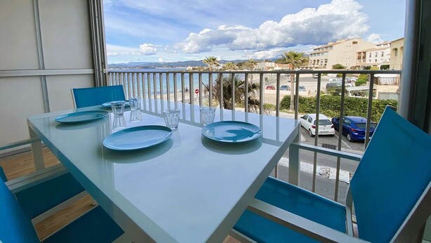 Un balcon avec une table dressée pour deux personnes, donnant sur une zone côtière avec des bâtiments et des voitures.