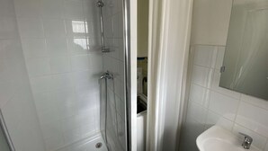Une salle de bain avec des murs recouverts de carreaux blancs, une douche en verre, un lavabo blanc et un miroir.