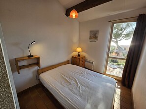 Ett sovrum med en säng, ett skrivbord med en lampa, ett element och ett fönster med gardiner.