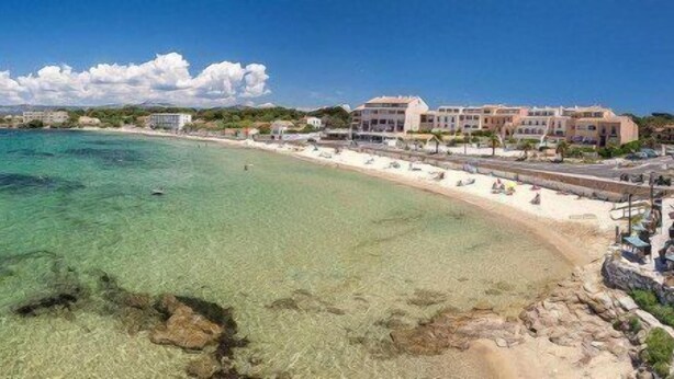 Un hotel sul lungomare con vista sulla spiaggia, acque cristalline e un litorale roccioso.
