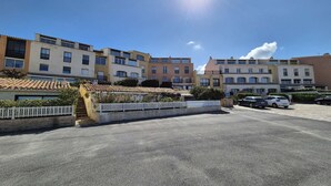 Un parcheggio con diverse auto, una recinzione bianca a picco e palazzi a più piani con balconi.