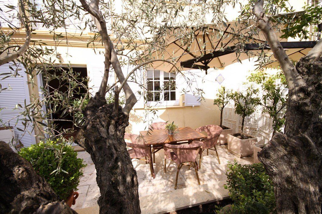 An outdoor patio with a round table and chairs, surrounded by trees and potted plants.