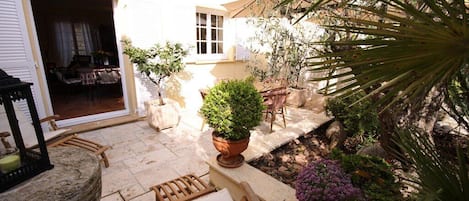 Une terrasse extérieure avec un sol en pierre, une chaise en bois, une plante en pot et une petite table.