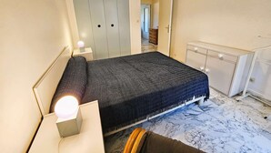 Ein Schlafzimmer mit Bett, Nachttisch, Lampe, Kleiderschrank und Pendelleuchte.