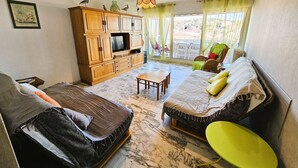 Ein Wohnzimmer mit einer Couch, einem Holzschrank, einem Fernseher und einem Esstisch.