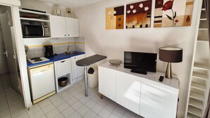 Een keukentje met een magnetron, koffiezetapparaat en een klein spoelgedeelte. Er is een televisie op een witte kast en een lamp op een bijzettafeltje.