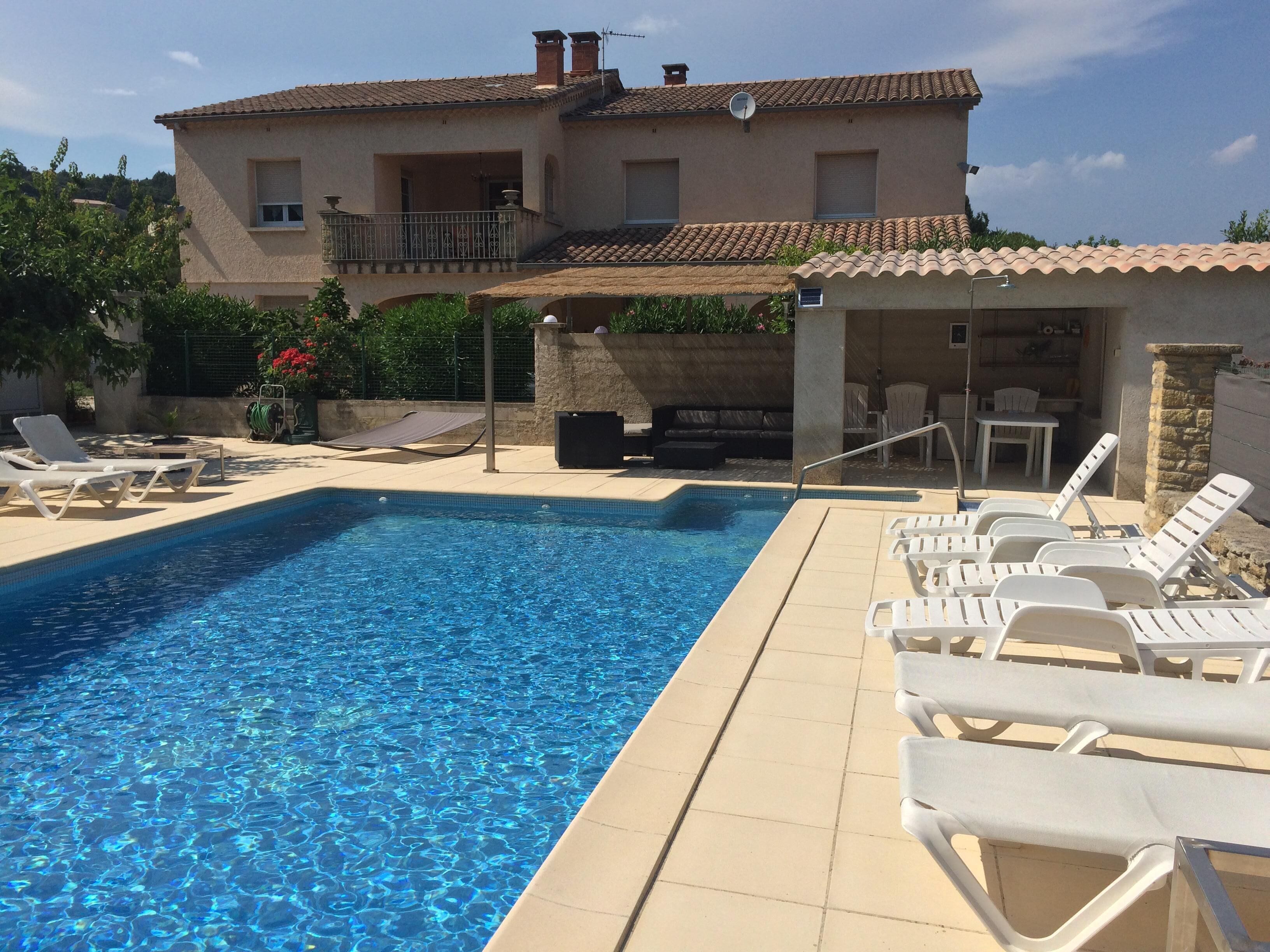 A swimming pool with lounge chairs, a covered seating area, and a building with a tiled roof.