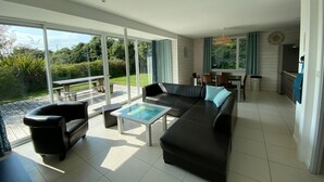 A spacious living room with a black leather sofa, a glass coffee table, and a dining area with a table and chairs.