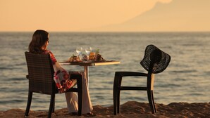 Une personne est assise à une table, avec une vue sur la mer et une montagne en arrière-plan.
