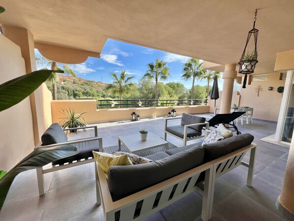 A spacious outdoor patio with a dining area, seating, and a view of palm trees and hills.