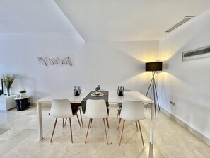 A modern dining area with a white table, four white chairs, a floor lamp, and abstract wall art.