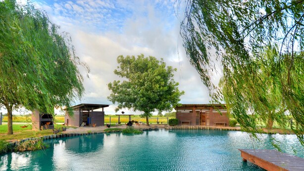 Un área de piscina exterior tranquila con estructuras de madera, rodeada de exuberante follaje y árboles.