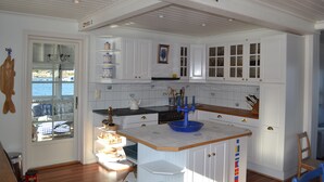 Una cocina con armarios blancos, una isla de madera y vistas a través de un ventanal.