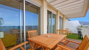 A wooden deck with a table and chairs, large sliding glass doors, and a view of the sea. - Tulette-2040-Convenient apartment with view (Cannes)