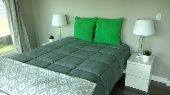 A neatly made bed with a patterned bedspread, a green quilted headboard, and two bedside tables with lamps and small potted plants. - Newly designed waterfront away (Fremont)
