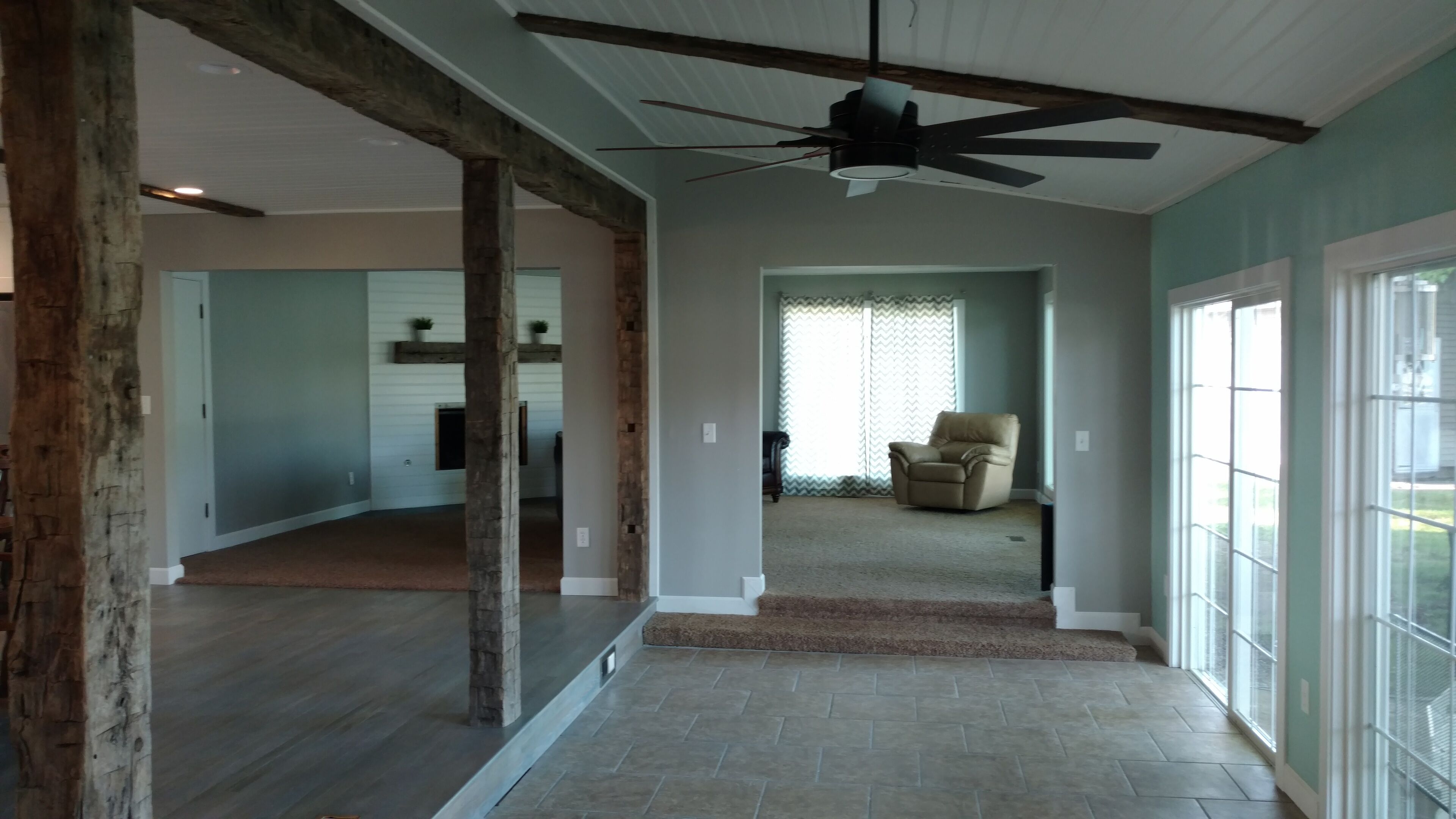 A spacious interior with a high ceiling, exposed wooden beams, a ceiling fan, and a view to the outside through large windows.