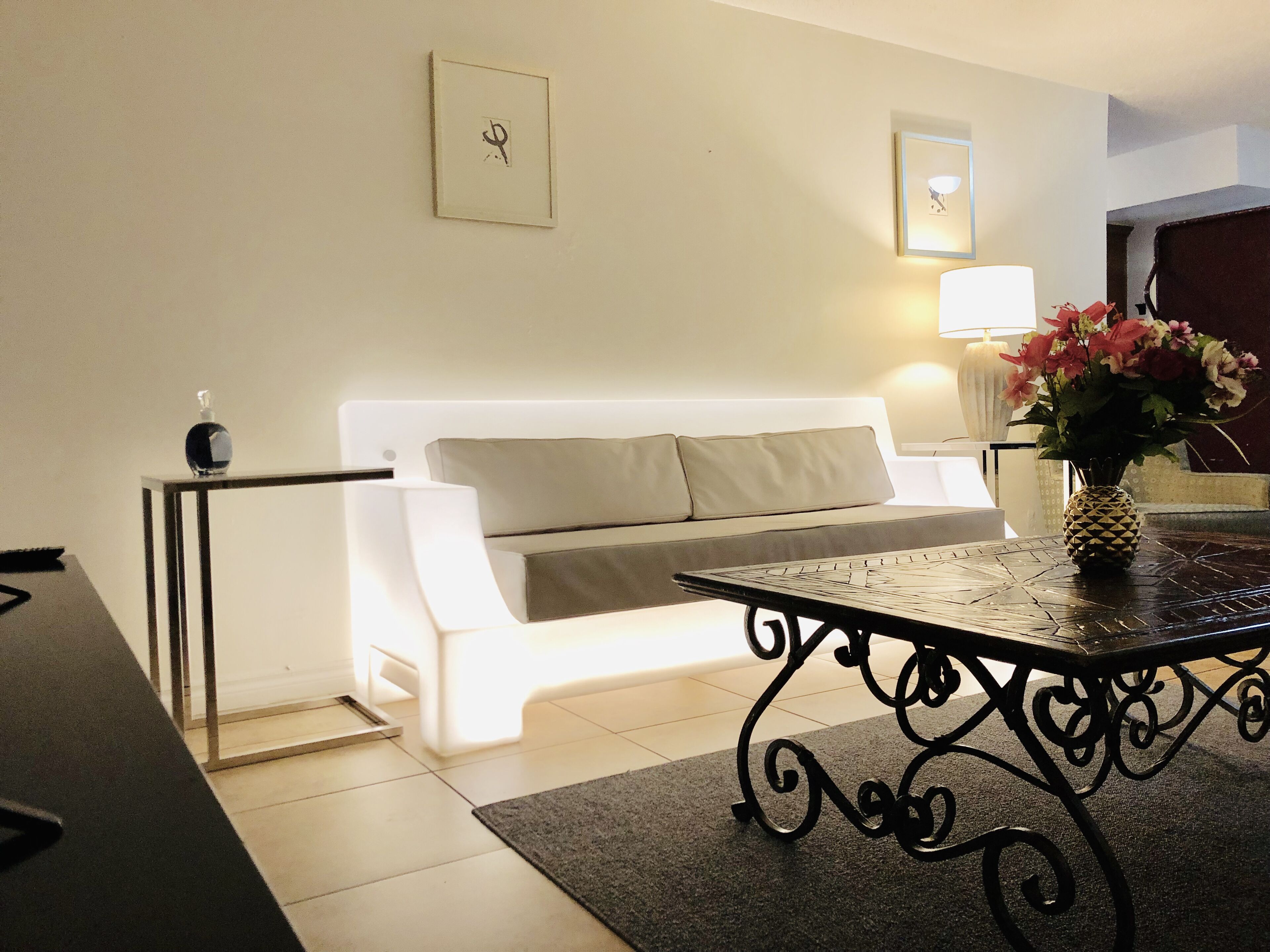 A modern living room with a white sofa, a black coffee table with a pineapple centerpiece, and a small side table.