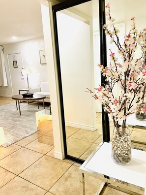 A modern hotel room with a large mirror, a vase with pink flowers, a white sofa, and a small table with a lamp. - 3BR condo Strip nearLVCC LasVegas Sphere best spot sale Sema Show (Las Vegas)