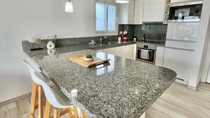 Una cucina moderna con isola in granito, sgabelli di legno, lavello in acciaio inossidabile ed elettrodomestici integrati.